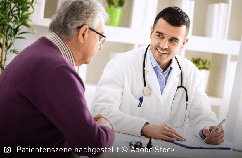 Freundlich lächelnder junger Arzt schaut seinen älteren Patienten aufmunternd an: Mastozytose ist nicht heilbar, die Symptome lassen sich aber lindern.